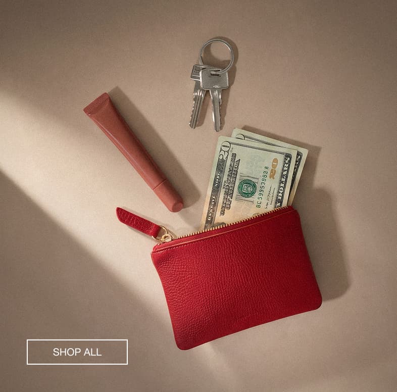 Alt Text: Red leather zip pouch styled with cash, keys, and a lip product on a neutral background.  CTA Copy: SHOP ALL