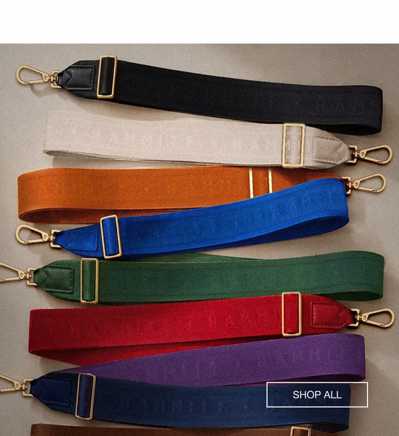 Assortment of wide webbed crossbody straps arranged in black, cream, orange, blue, green, red, purple, and navy with gold hardware.  CTA Copy: SHOP ALL
