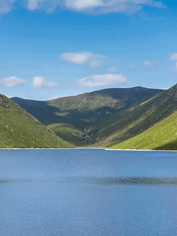 A serene lake surrounded by lush green hills under a clear blue sky.