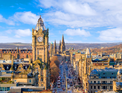 A panoramic view of a city street featuring a clock tower and historic buildings under a blue sky.