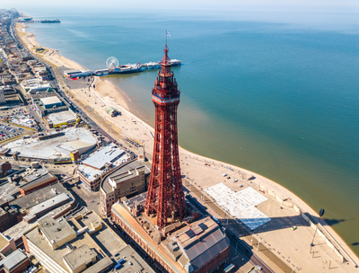 Aerial view of Blackpool Tower beside the coastline, with the beach and pier in the background.