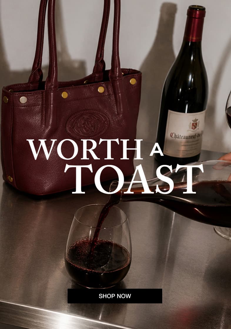 Wine-toned pebble leather tote with gold rivets displayed beside a bottle and glass of red wine.  Image Copy: WORTH A TOAST  CTA Copy: SHOP NOW