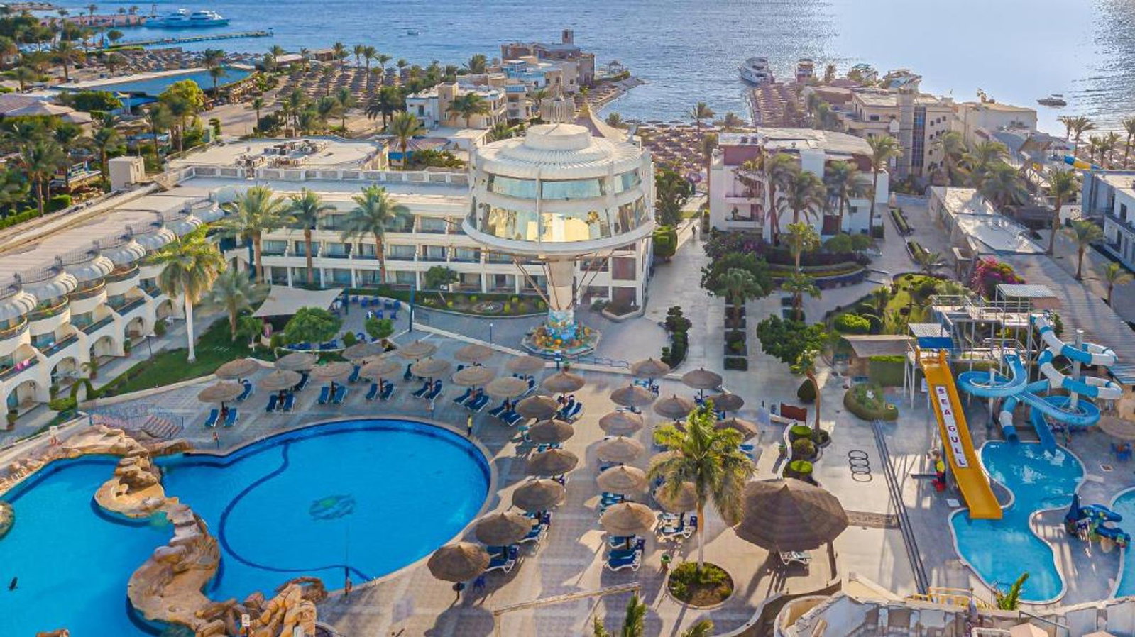 Aerial view of a seaside resort with large swimming pools, sunloungers and straw parasols, water slides and yachts along the coastline