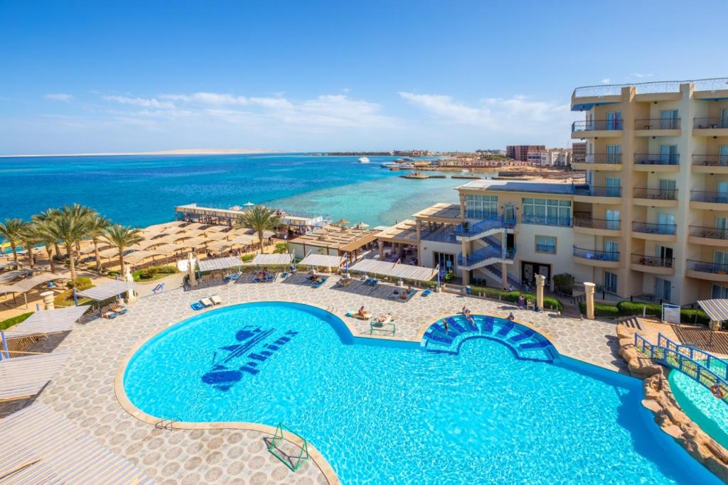Aerial view of a seaside resort with large turquoise swimming pool, sun loungers, palm trees and sandy beach on a clear sunny day