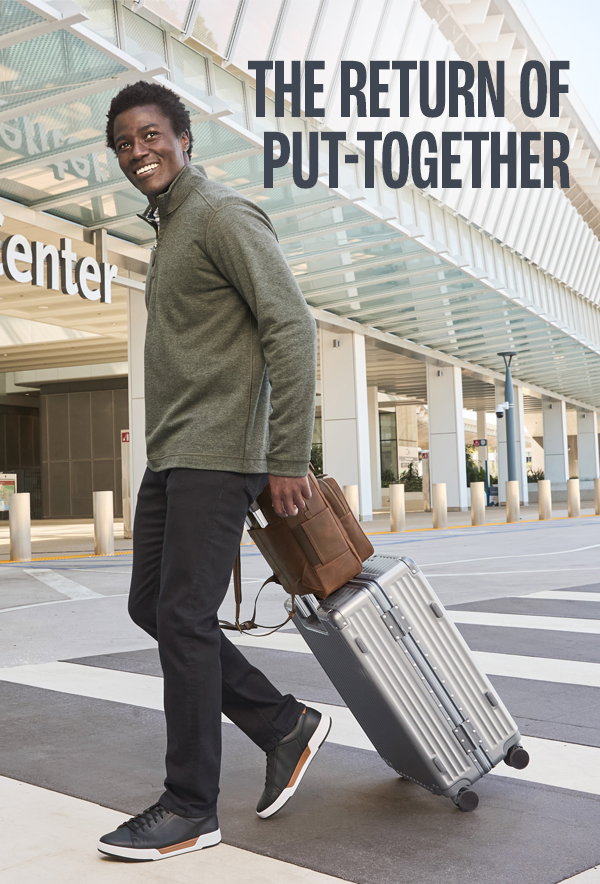 Model wearing a green quarter-zip, black pants, and black sneakers while walking with luggage outside an airport. Text reads: 