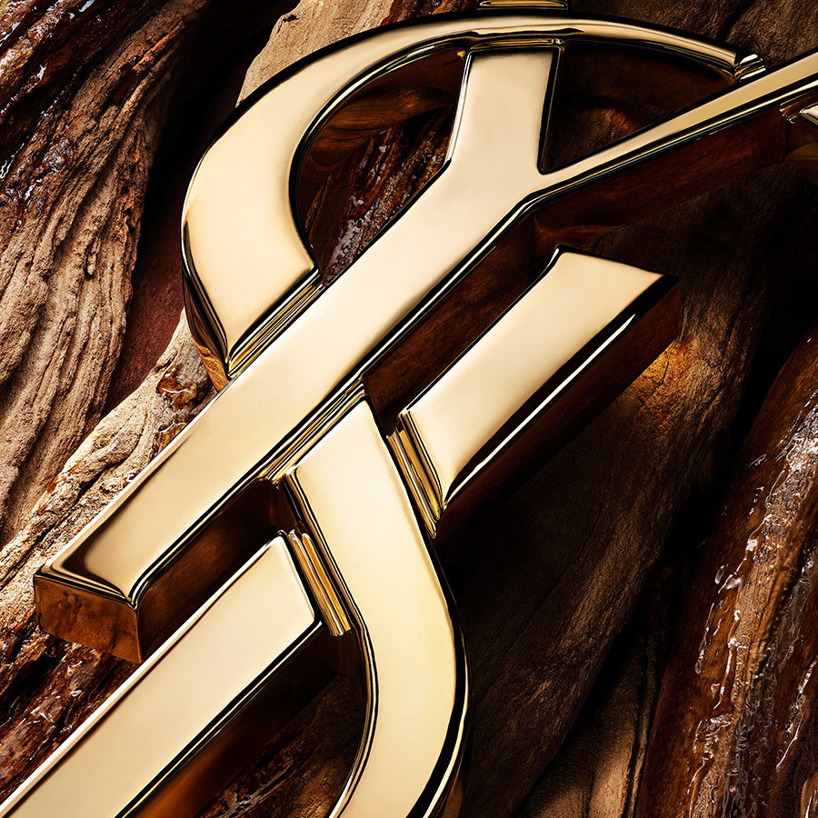 A close-up of a sculpted golden YSL logo lying on rich, warm polished wood.
