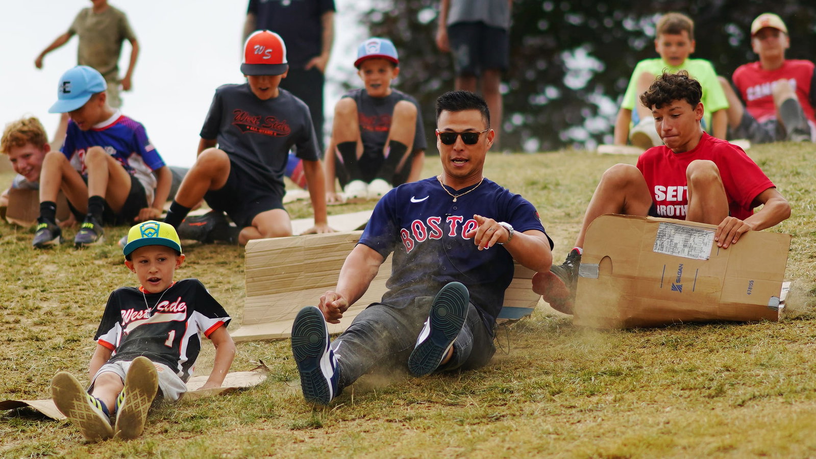 Former Red Sox player Rob Refsnyder slides down a hill alongside kids