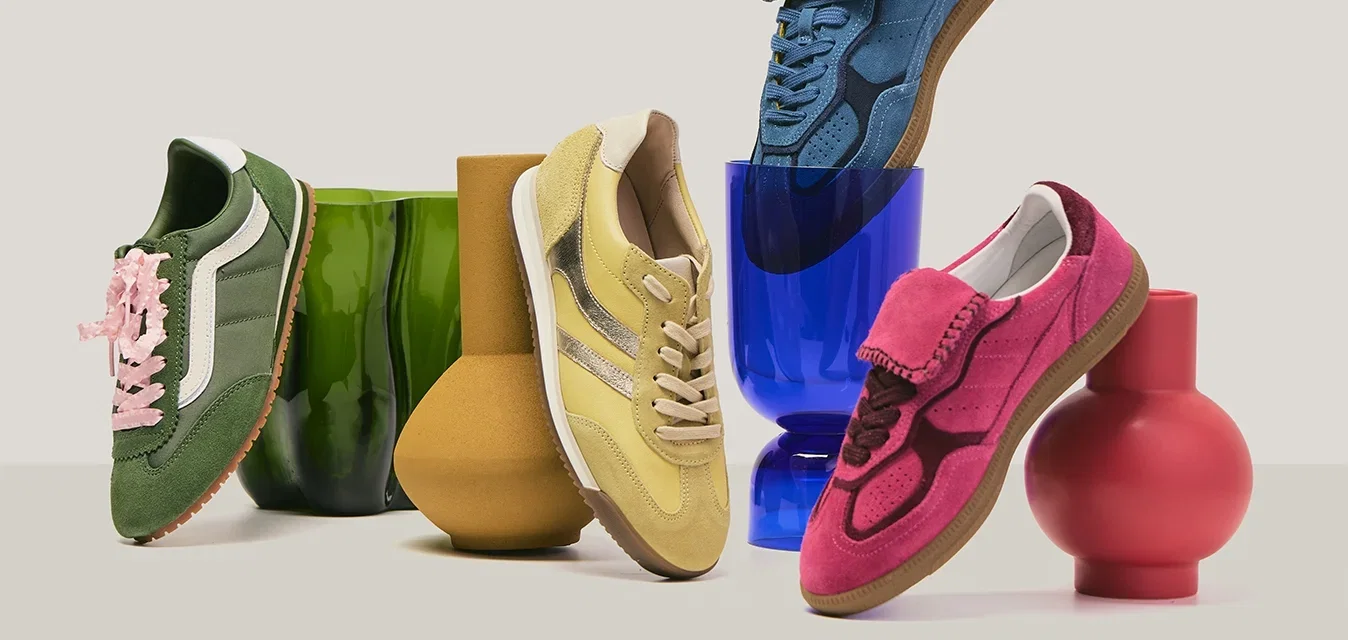 Vier farbenfrohe Sneakers in Grün, Gelb, Blau und Pink, arrangiert auf und um einzigartig geformte grüne, braune, blaue und rote Vasen.