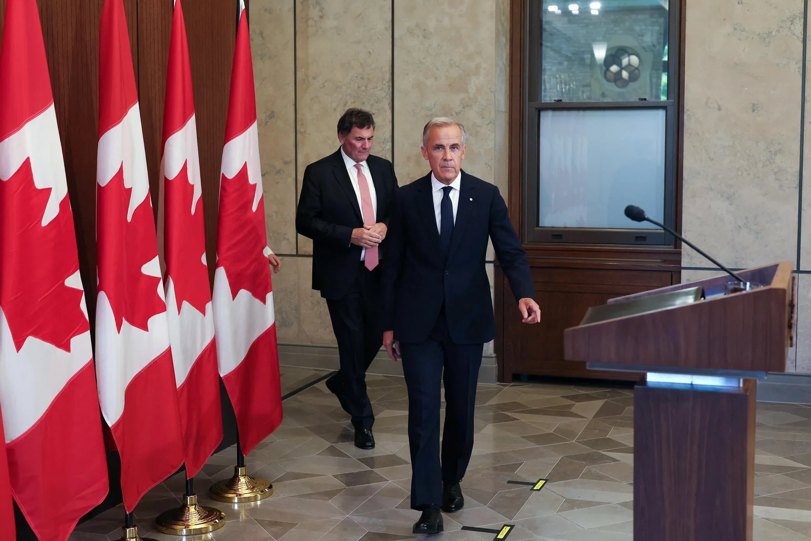 Mark Carney stepping up to a podium with four Canadian flags beside him