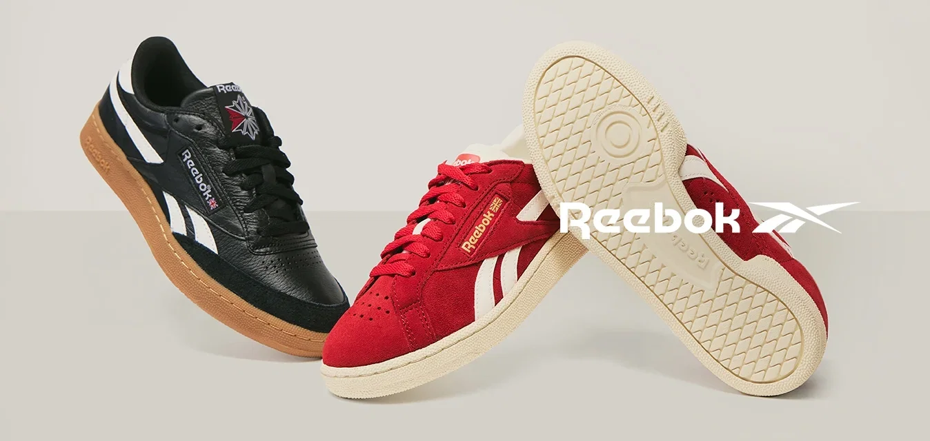 Schwarze Leder- und rote Wildlederschuhe von Reebok, nebeneinander gezeigt. Ein roter Schuh zeigt die Sohle mit strukturiertem Muster.