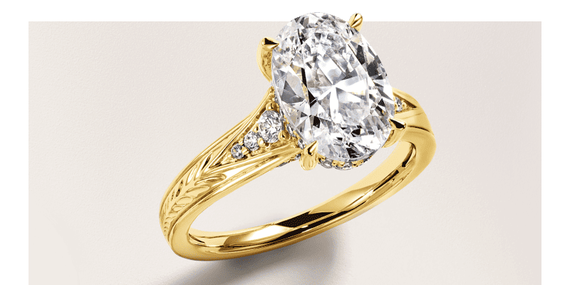 Yellow gold engagement ring with oval diamond, side diamonds and engraved band details.