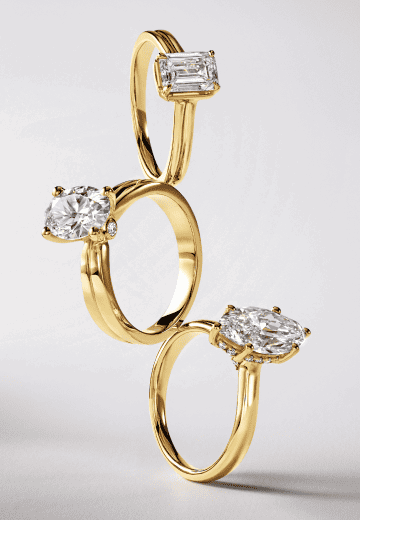 Three stacked yellow gold solitaire rings with emerald, round and marquise diamonds.