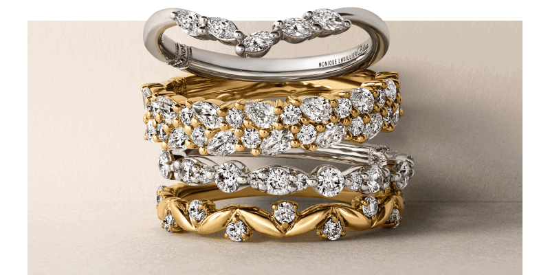 Stack of five white and yellow gold diamond wedding bands in mixed designs.