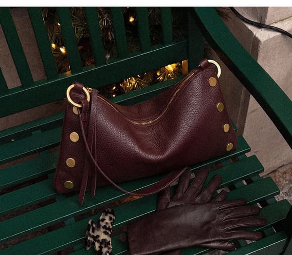 Kyle bag in Cherrywood Pebble with gold rivets styled on a green bench with coordinating leather gloves.