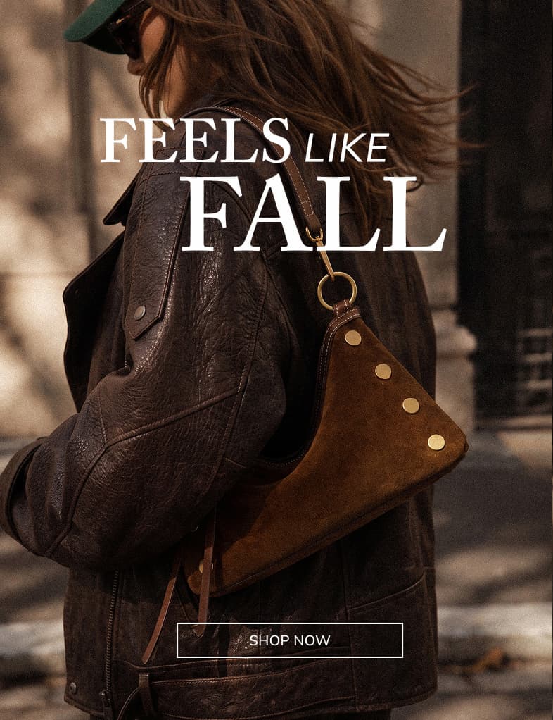 FEELS LIKE FALL Alt Text: Model wearing a Kyle shoulder bag in Cinnamon Suede with gold rivets and brown leather trim over a dark brown jacket.