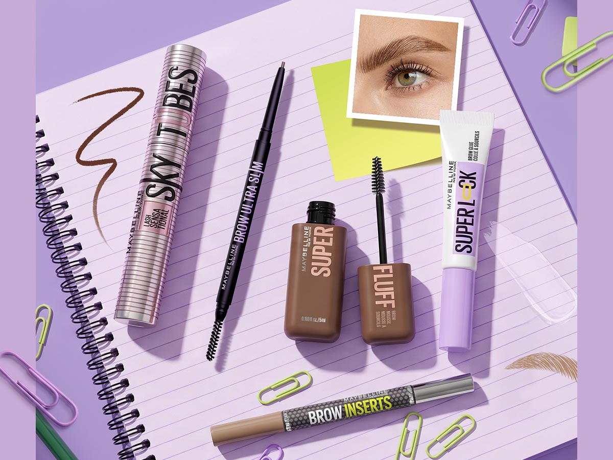 Maybelline eyebrow products arranged on a lined notebook with colorful paper clips, a close-up brow photo, and visible brow-pencil strokes and product textures—bringing a Back-to-School theme to the brow routine.