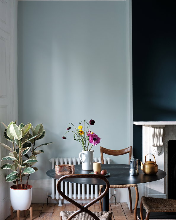 Dining corner painted in a soft pale blue-grey, with a wooden table, fresh flowers and potted plants illuminated by natural light, highlighting Borrowed Light No.235.