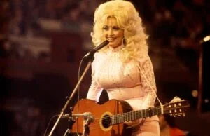 American singer, songwriter and actress Dolly Parton, performs with a guitar, 1976.