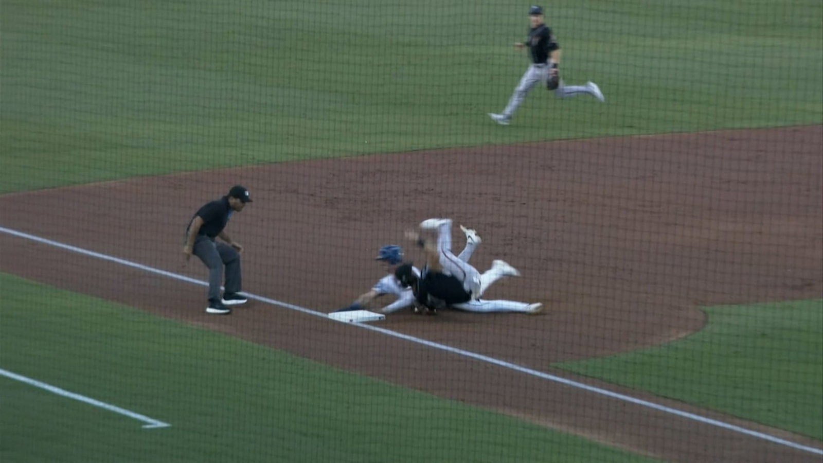 A screengrab of a third baseman tumbling onto his back as a runner slides into the base
