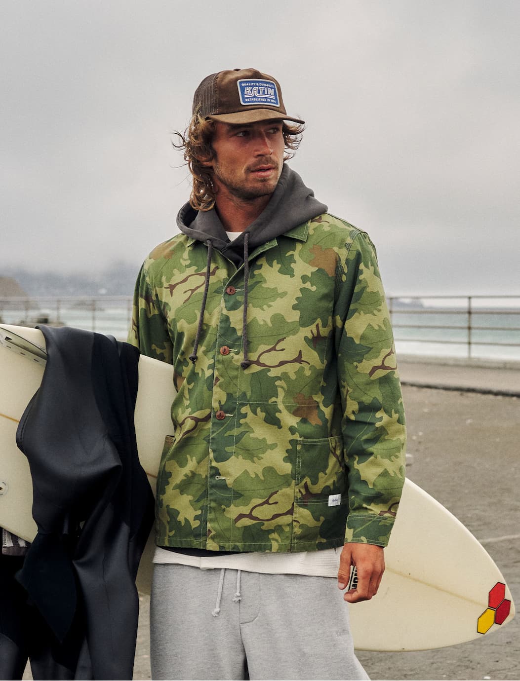 Katin Camo Task Jacket on surfer standing looking at ocean holding his surfboard