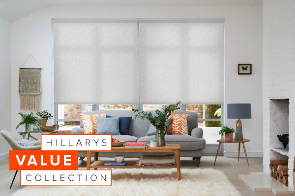 Bright living room with two large windows dressed in light patterned Roller blinds behind a grey sofa and wooden coffee table.