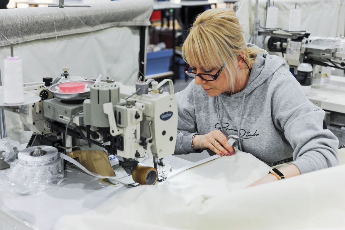 Person operating an industrial sewing machine, carefully guiding fabric through equipment in a busy textile workshop