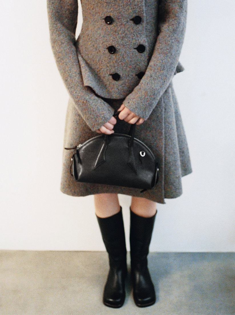 Cropped image of model wearing the Capucine Jacket in Donegal Knit in Blue multi with the Capucine Skirt in Donegal Knit in Blue multi, holding the Small Bowler Bag in Shiny Goat in Ebony anf wearing the Esme Boots in Shiny Calf in Black