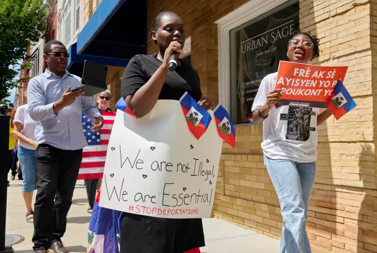 A woman walks while holding a microphone and a poster decorated with Haitian flags and the text 