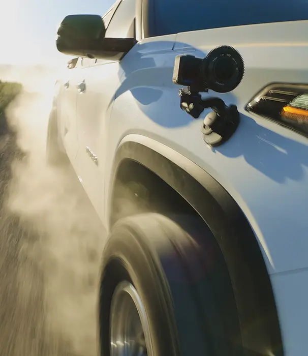 GoPro camera mounted on the side of a white truck driving on a dirt road.