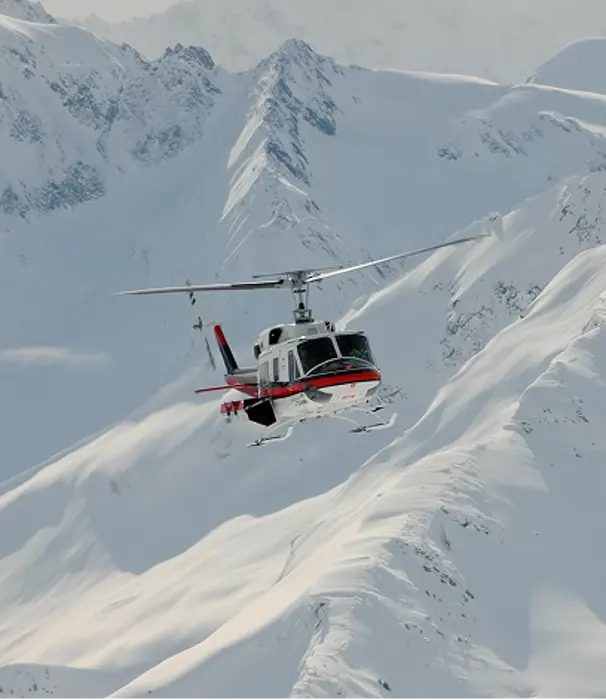 A red and white helicopter flying over snowy mountains.