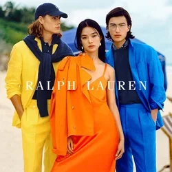 Drei Models stehen am Strand. Eine trägt einen gelben Anzug mit einem Marineblauen Pullover, die zweite ein oranges Kleid mit passender Jacke und die dritte einen blauen Anzug.