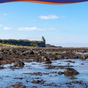 Coastal landscape featuring rocky shorelines and a distant tower under a clear blue sky.