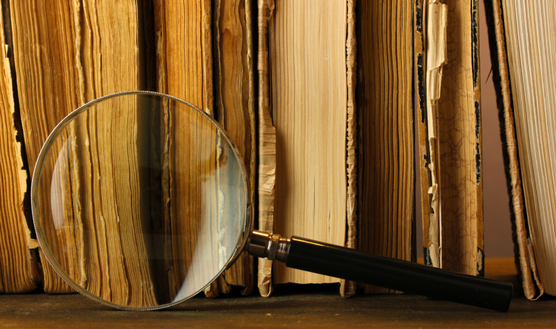 A magnifying glass rests against a row of old, weathered books with yellowed pages and worn covers.