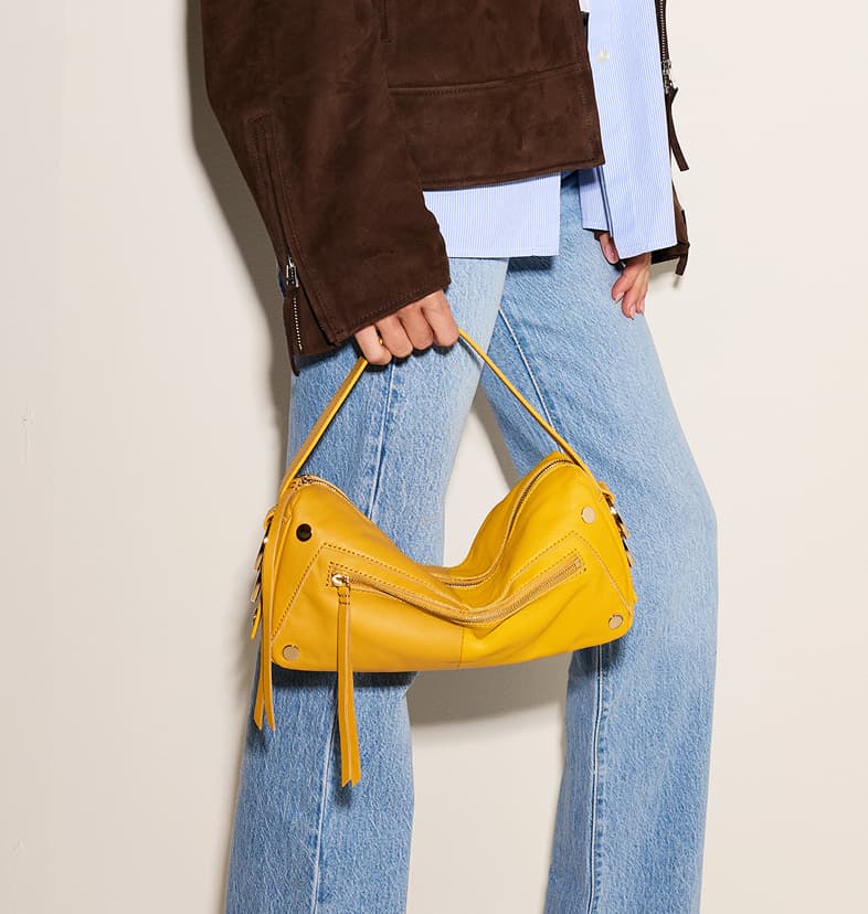 Model wearing light-wash jeans and a brown suede jacket, carrying a Double Yellow leather Doxie bag with gold hardware.