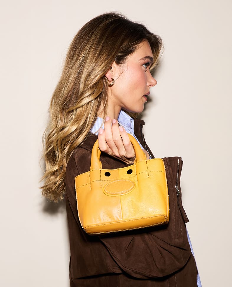 Model in a brown suede jacket carrying a small Double Yellow Olympia with top handles and gold hardware.
