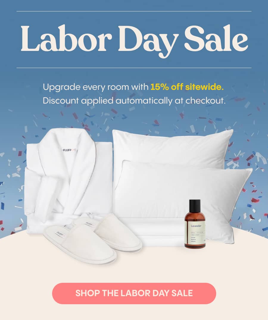 A medium shot displays a white bathrobe, two white slippers with 'FLUFF' printed on them, white pillows and sheets, and a small brown bottle labeled '...