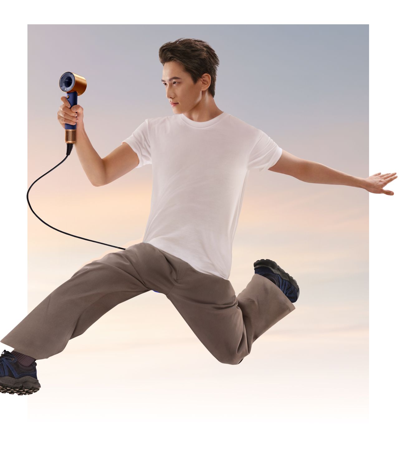 A jumping model in mid-air holding the Dyson Supersonic Travel hair dryer.