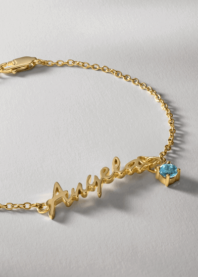 Yellow gold name script bracelet with blue gemstone charm.
