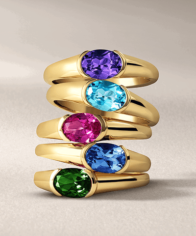Stacked yellow gold gemstone rings featuring colorful oval-cut center stones.