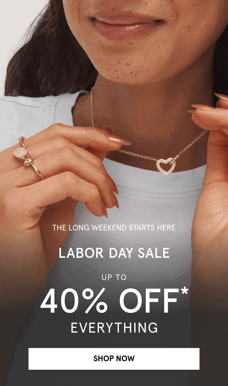 Woman wearing gold rings and holding a diamond heart pendant necklace. Labor Day sale. Click shop now.