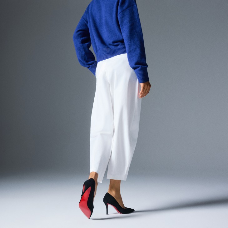Woman in dark sweater and white pants wearing black high heels.
