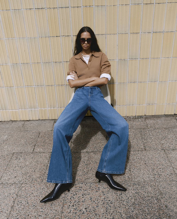 Woman sitting wearing Wide-Leg Jeans in Mid Blue and Rugby Top in Caramel with Chelsea Boots in Black