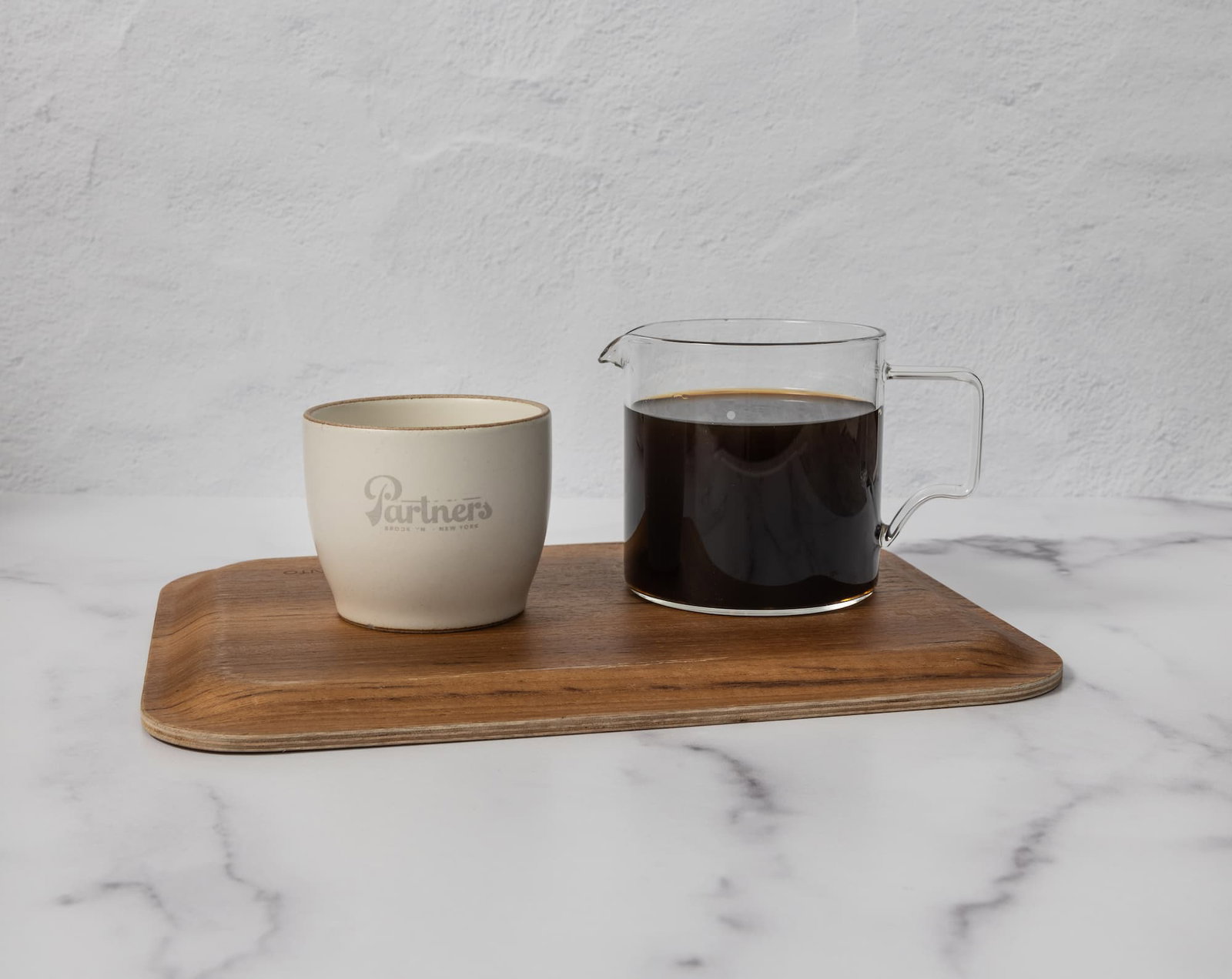 A Partners Coffee pour over cup and carafe filled with coffee displayed on a wooden tray