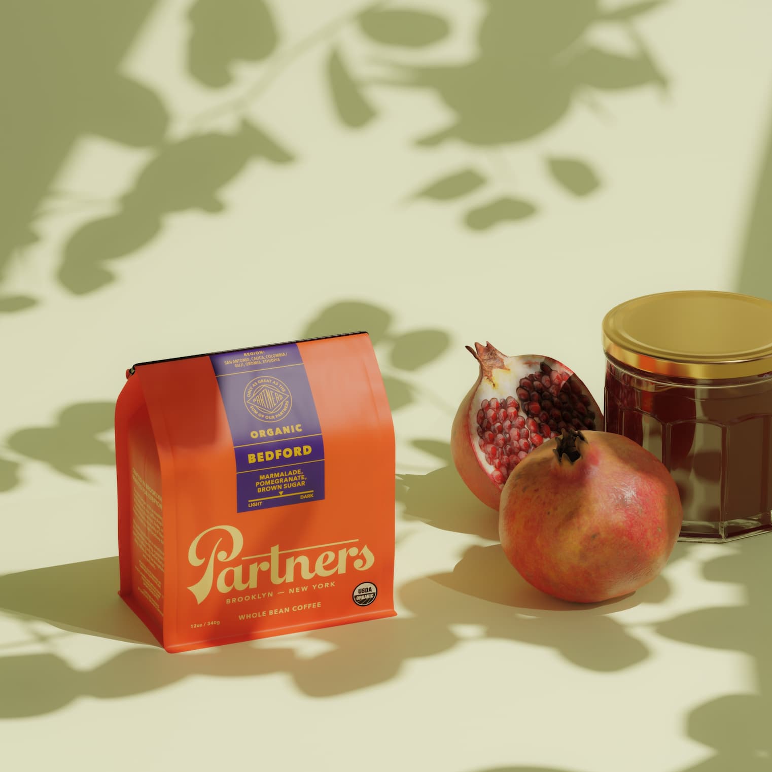 A Bag of Partners Coffee Bedford - Organic with pomegranates and a jar of marmalade on a sunny backdrop shadowed by tree branches.