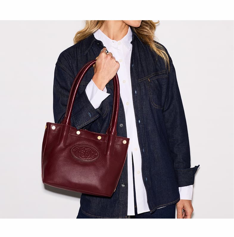 Model in a dark denim jacket carrying a Olympia sml Cherrywood Pebble leather tote with gold hardware.