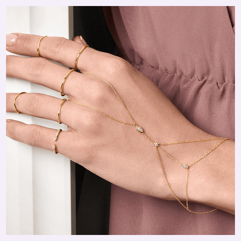 Focus on model’s dainty gold rings & hand chain with diamond accents. 
