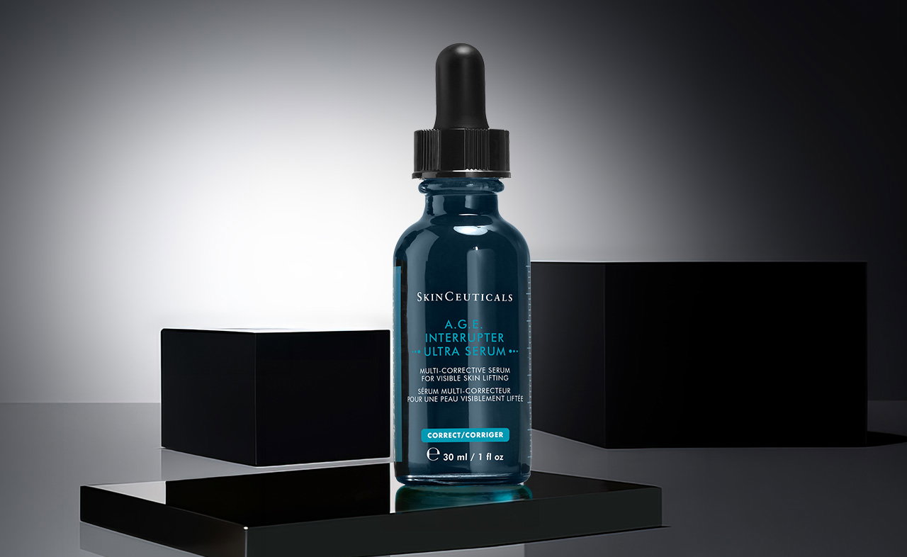 Eine einzelne SkinCeuticals A.G.E. Interrupter Ultra Serum-Flasche mit blauer Glasfarbe und schwarzem Pipettenverschluss auf einem schwarzen Podest mit zwei schwarzen Würfeln im Hintergrund.