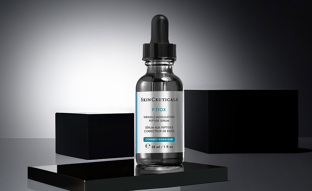 Eine einzelne SkinCeuticals P-TIOX Serum-Flasche mit klarem Glas und schwarzem Pipettenverschluss auf einem schwarzen Podest mit zwei schwarzen Würfeln im Hintergrund.