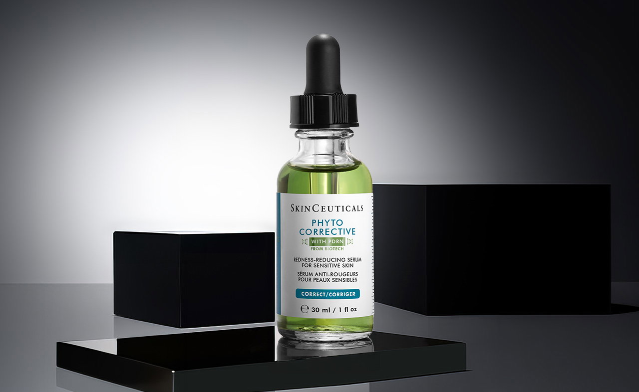 Eine einzelne SkinCeuticals Phyto Corrective PDRN Serum-Flasche mit grünlichem Inhalt und schwarzem Pipettenverschluss auf einem schwarzen Podest mit zwei schwarzen Würfeln im Hintergrund.