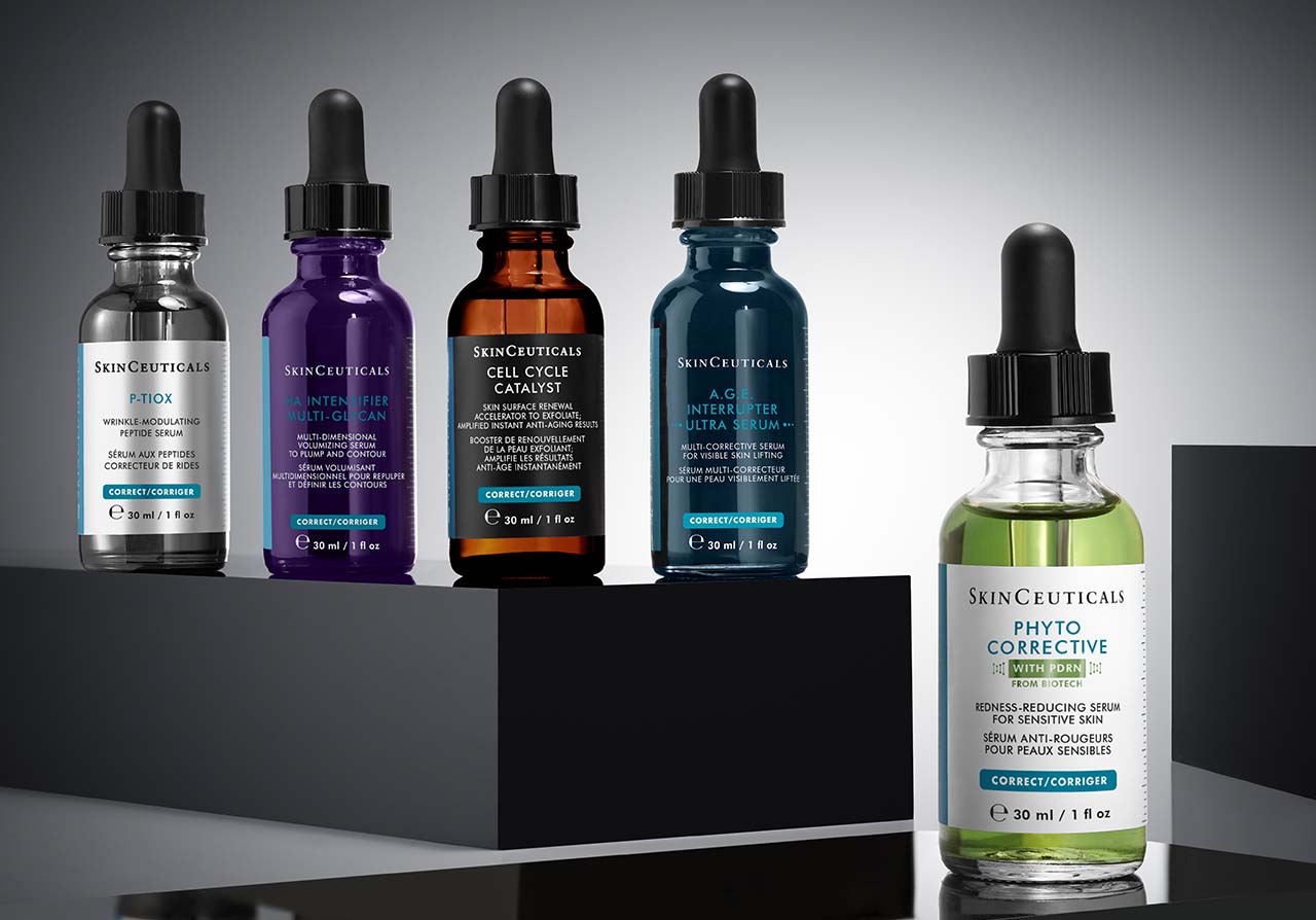 Fünf SkinCeuticals-Serum-Flaschen der Correct-Serie auf einem schwarzen Podest: P-TIOX Wrinkle-Modulating Peptide Serum, H.A. Intensifier Multi-Glycan Multi-dimensional Volumizing Serum, Cell Cycle Catalyst Skin Surface Renewal Accelerator, A.G.E. Interrupter Ultra Serum und Phyto Corrective Redness-Reducing Serum. Alle Flaschen haben schwarze Pipettenverschlüsse.